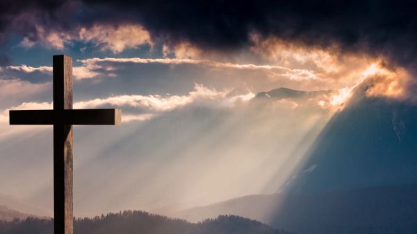 A cross silhouetted against sunbeams breaking through clouds